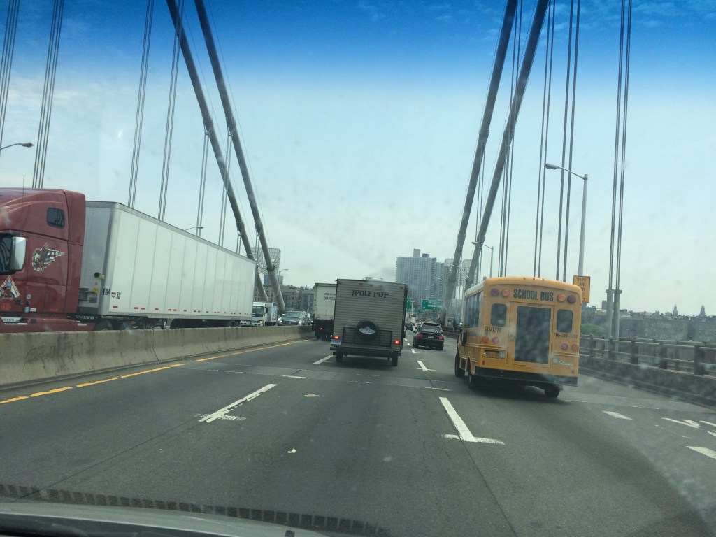 Traffic on a bridge featuring a red truck, a yellow school bus, and several other vehicles under a clear blue sky.