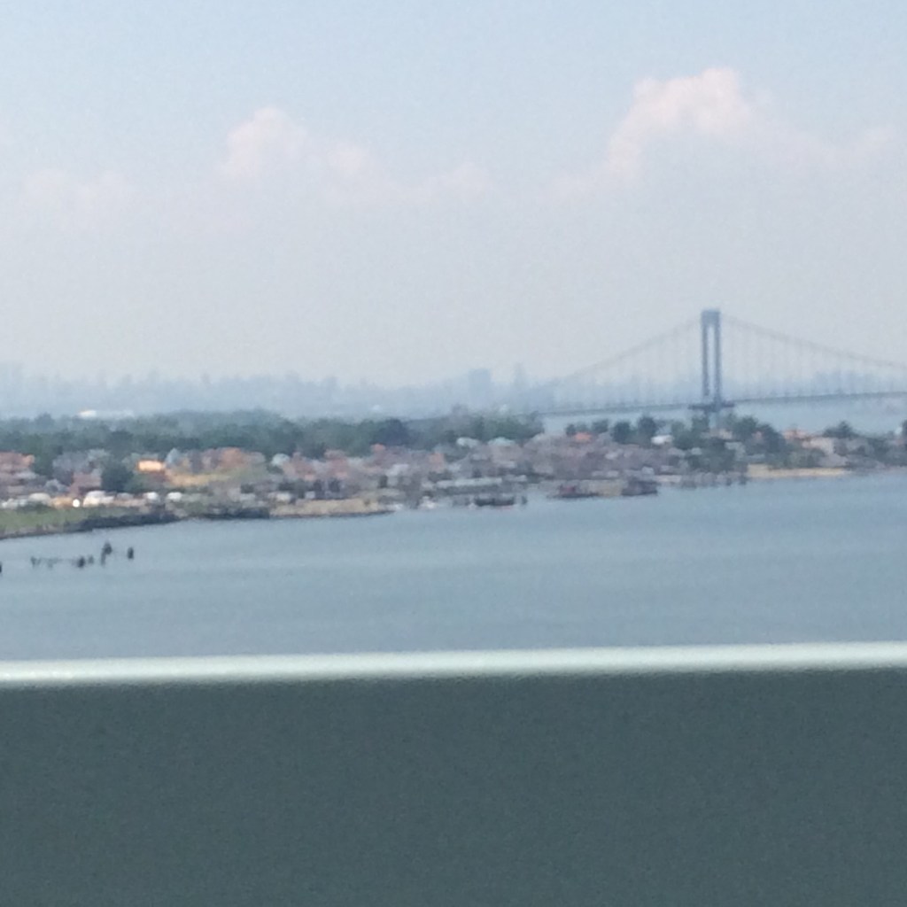 View of a river with a distant bridge and waterfront houses on a hazy day.