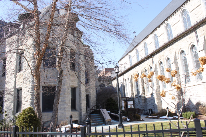 A scenic view of historic stone buildings with architectural details, surrounded by bare trees and a snow-dusted landscape.